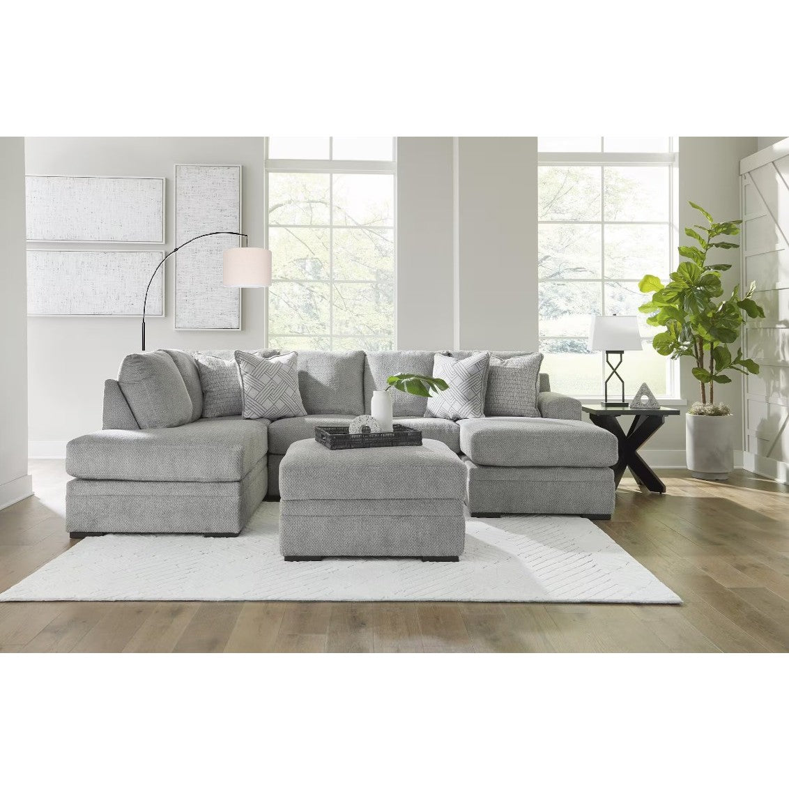Modern grey sectional sofa with ottoman in a bright living room with large windows.