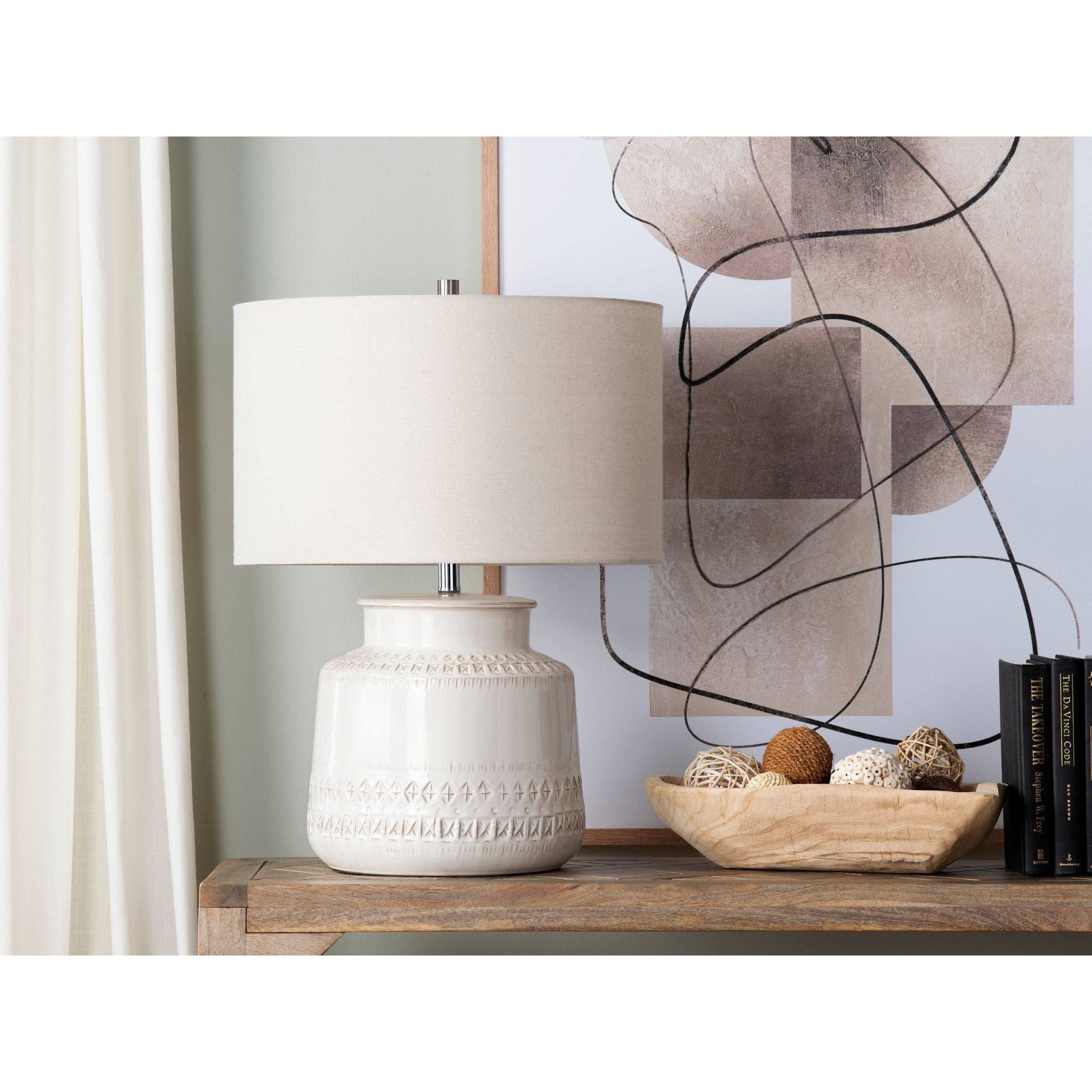 Ceramic table lamp with white shade on wooden console, next to decor and abstract art.