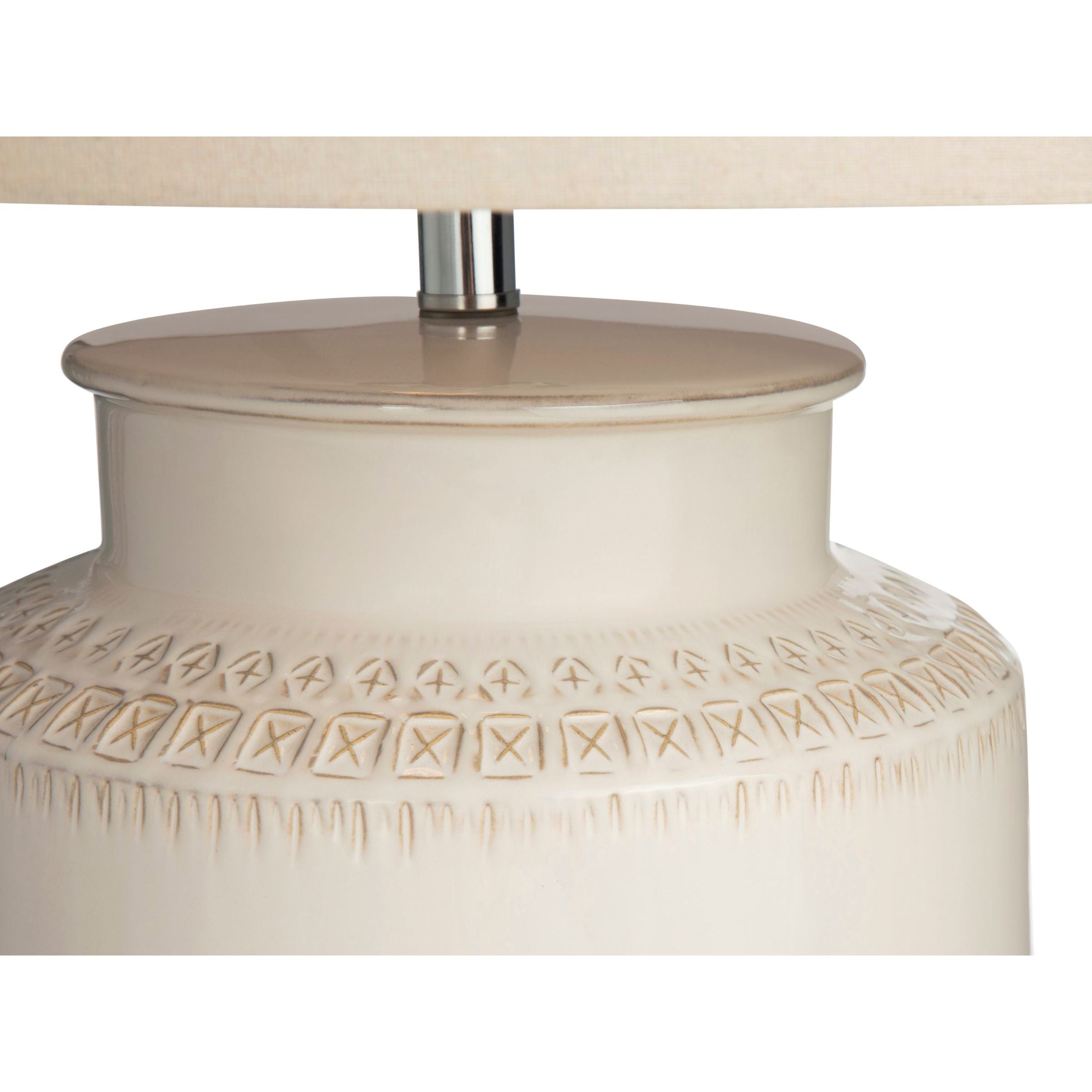 Close-up of a cream ceramic lamp base with geometric carved patterns.