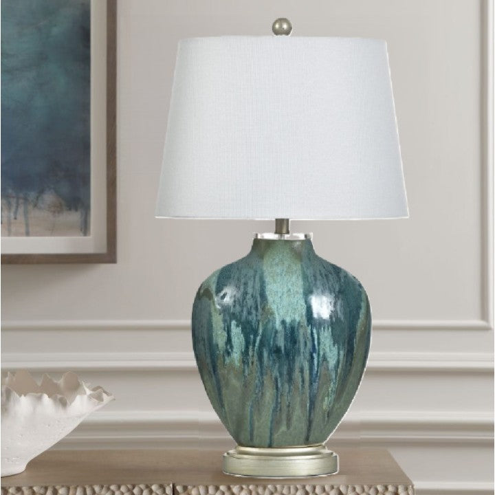 Table lamp with a blue and green ceramic base and white drum shade on a wooden console.