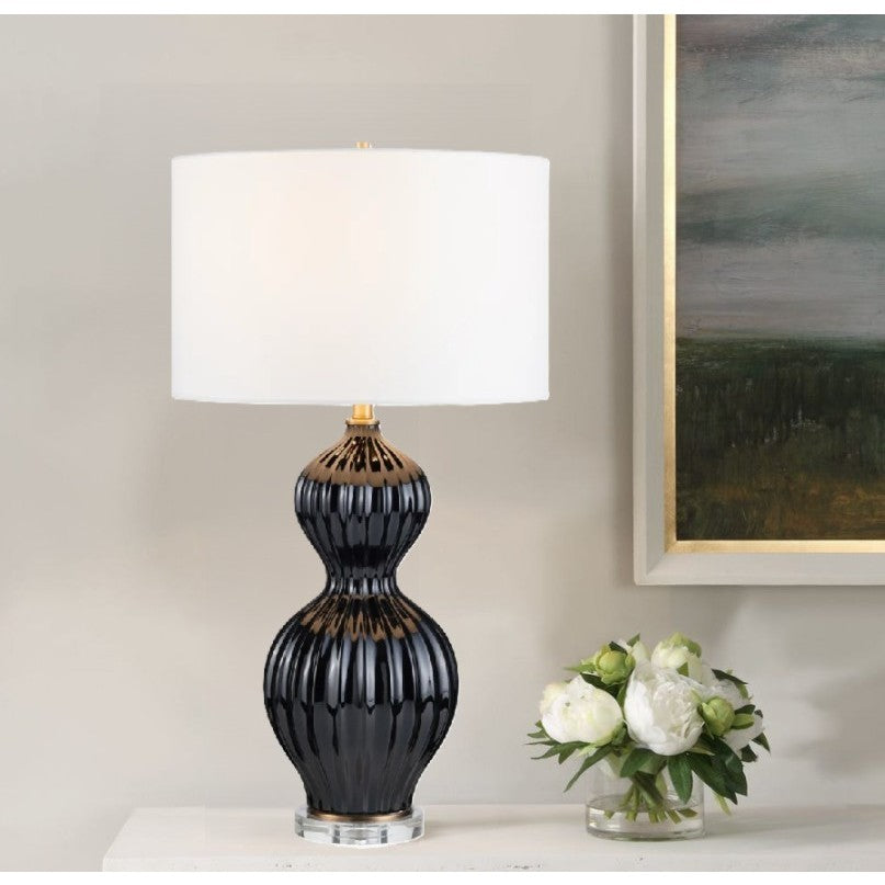 Black ceramic lamp with white shade on table beside white flowers.