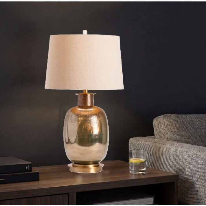 Gold table lamp with beige shade on a wooden side table next to a gray sofa.