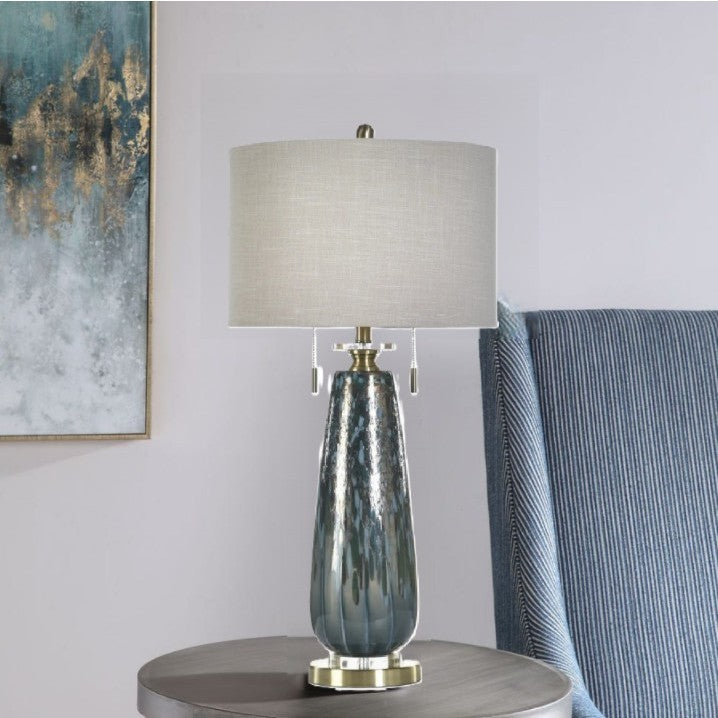 Modern table lamp with a textured blue glass base and white drum shade on a round side table.