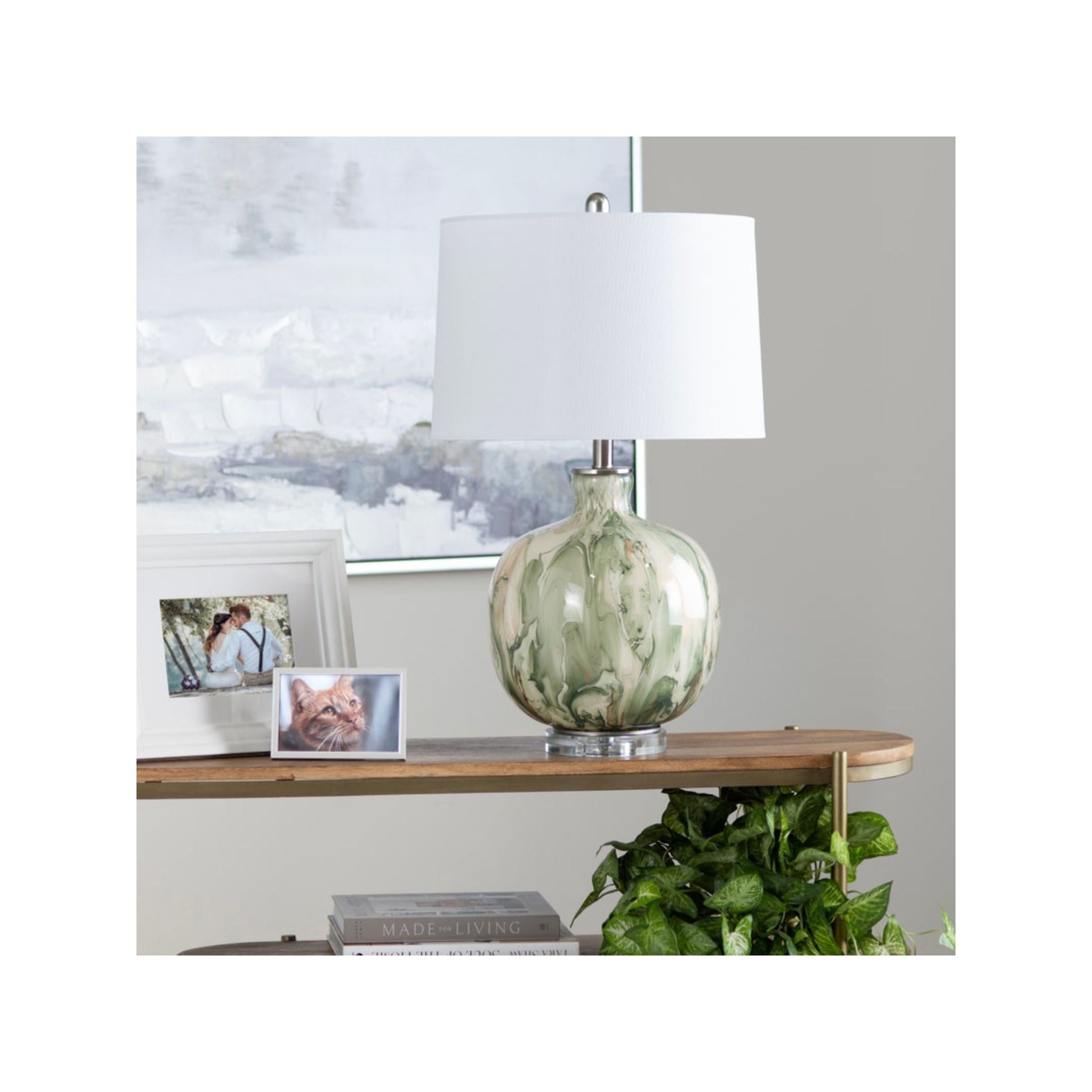 Green and white ceramic table lamp with white shade on a wooden shelf.