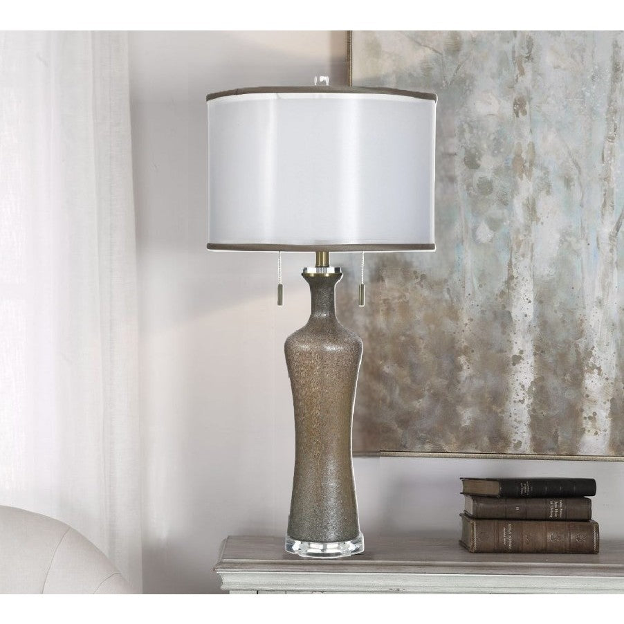 Tall ceramic table lamp with white shade on a console table next to stacked books.