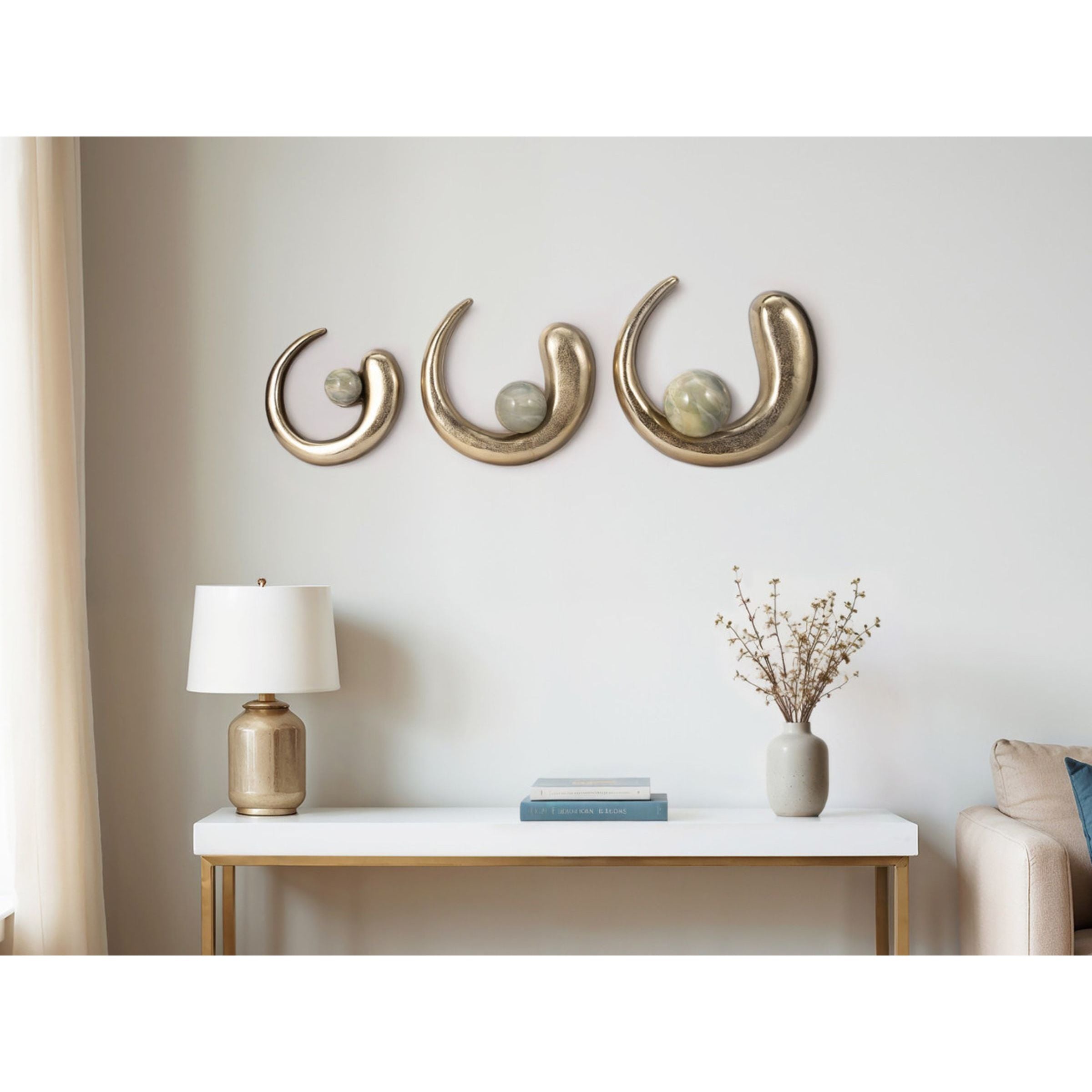 Modern living room with gold wall sculptures, lamp, books, and a vase on console table.