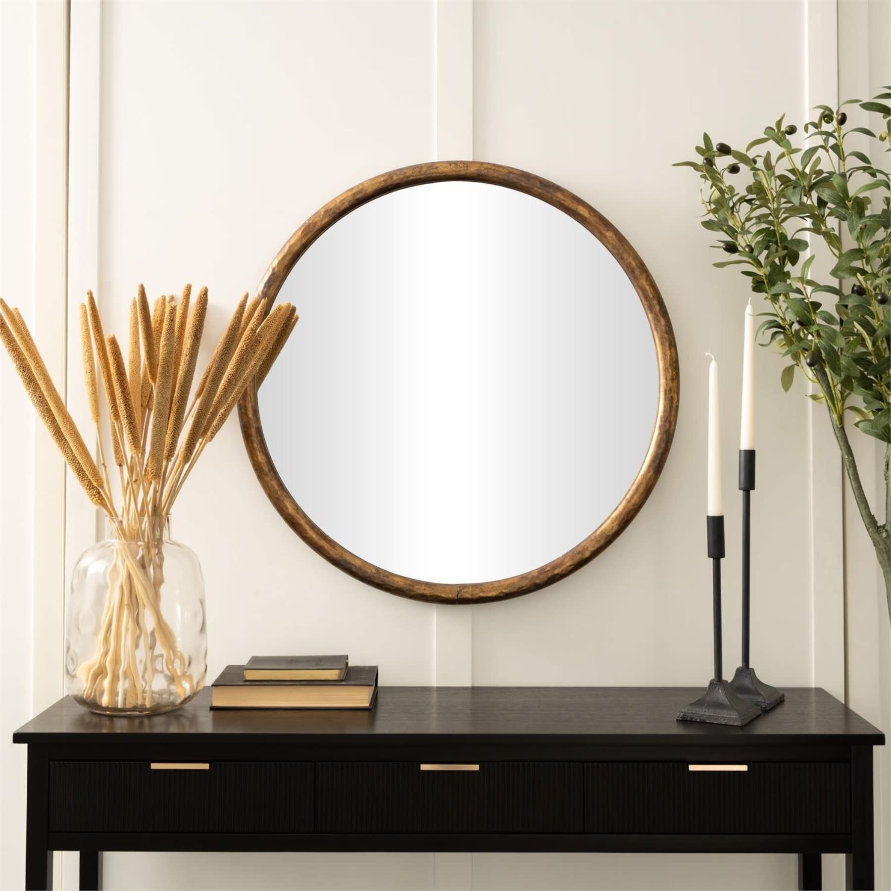 Round wall mirror with wood frame above a black console table with decor.