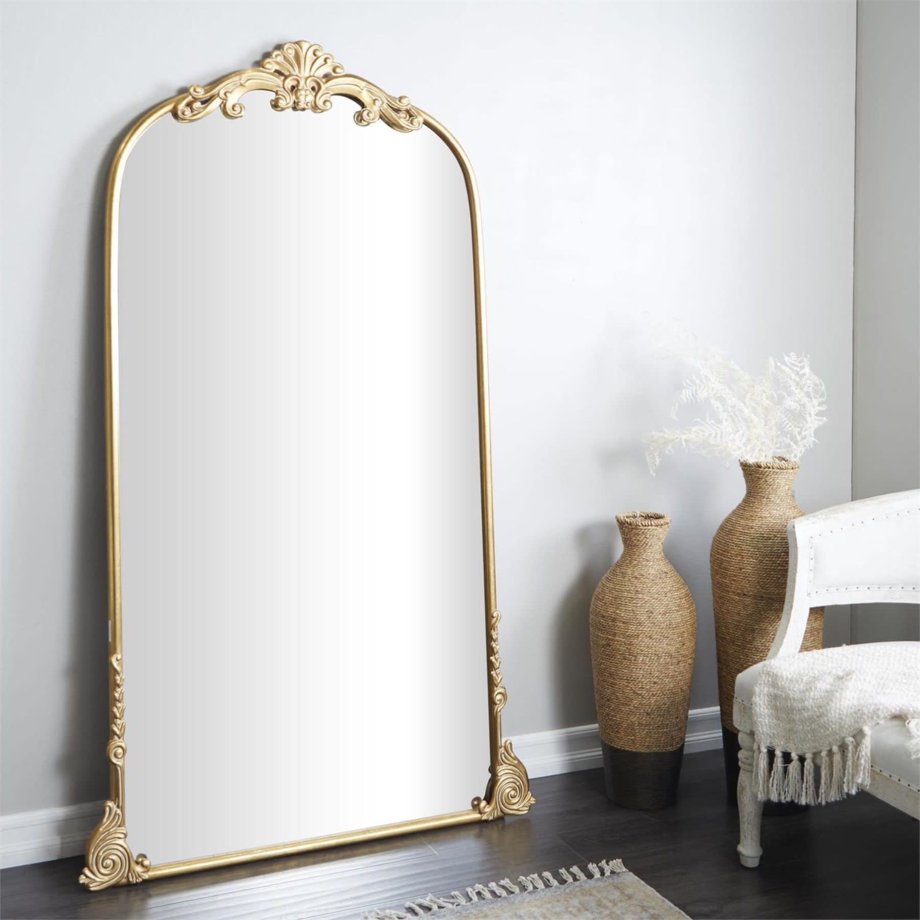 Tall gold-framed mirror with ornate top detail in a modern room setting.