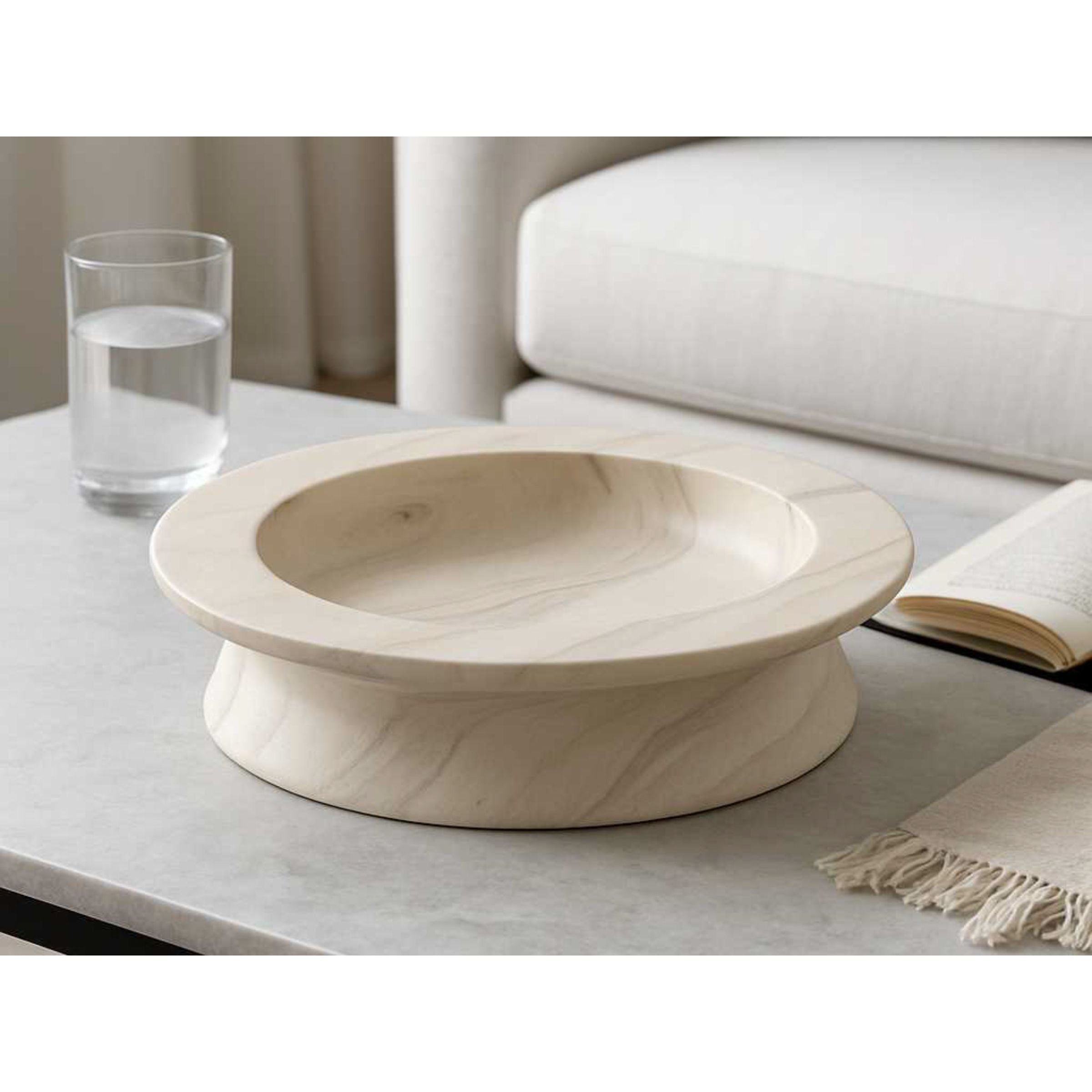 Round marble bowl on a coffee table next to a glass of water and an open book.