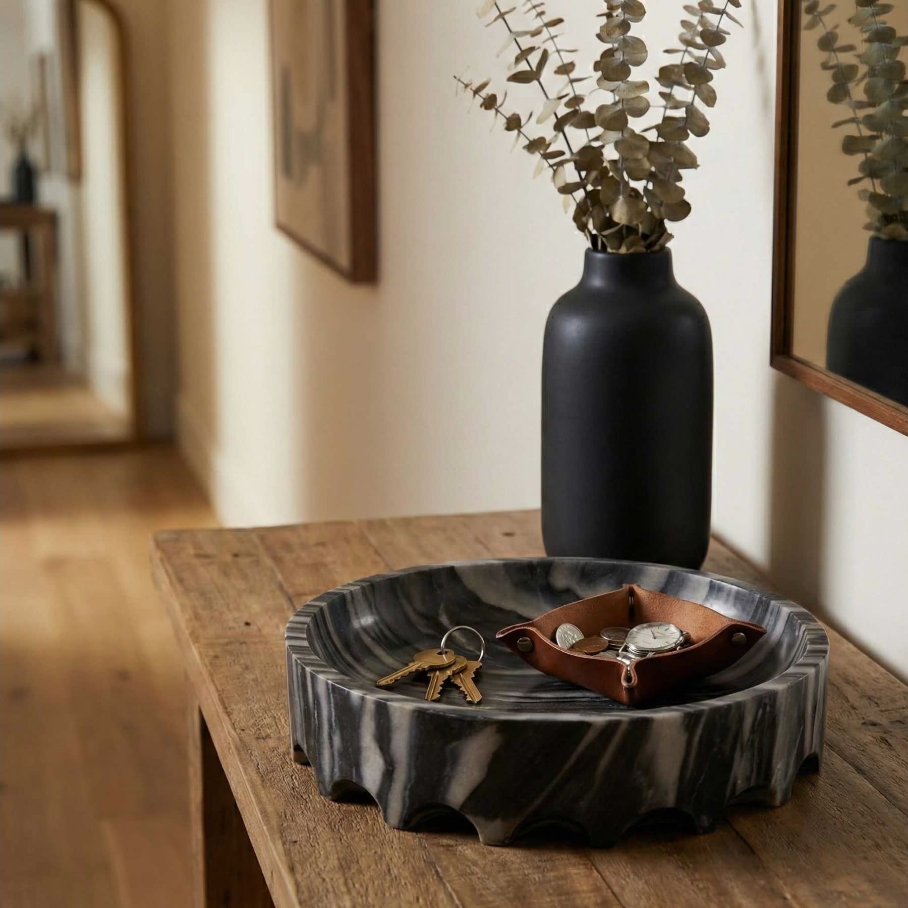 Wood console table with a black vase, dried branches, and a catchall tray with keys and coins.