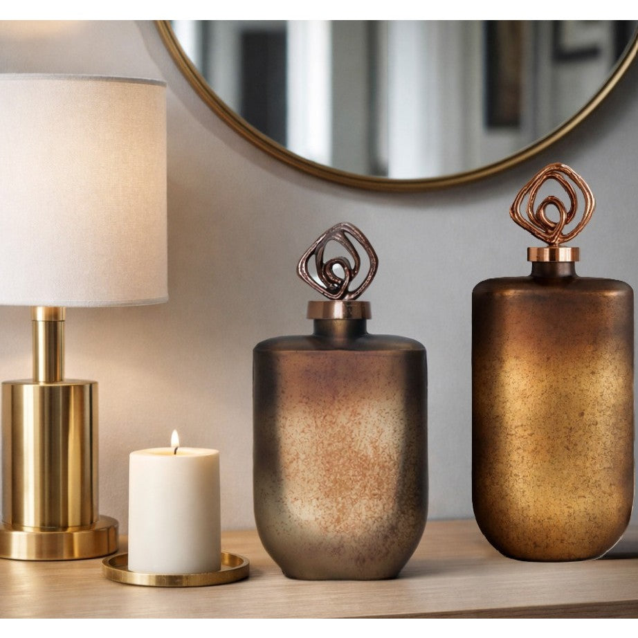 Modern decor scene with a gold lamp, white candle, and two metallic vases with artistic lids.