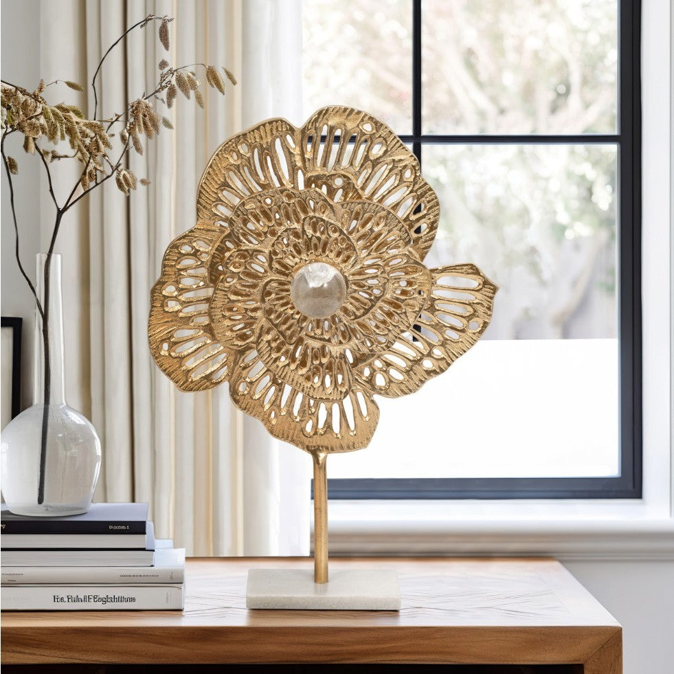 Gold floral metal sculpture on a stand displayed on a wooden table by a window.