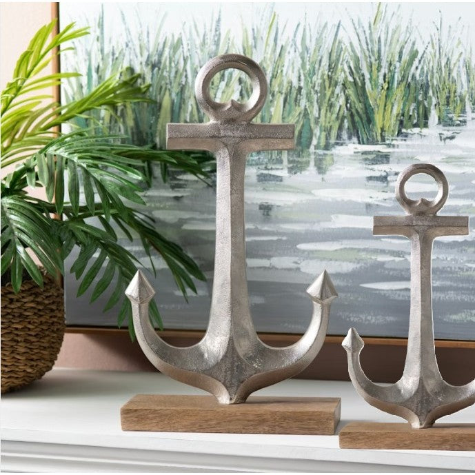 Silver anchor sculptures on wooden bases, with greenery and water scene artwork behind.