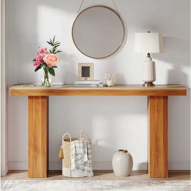 A modern wooden console table with a round mirror, lamp, books, and a vase of flowers.