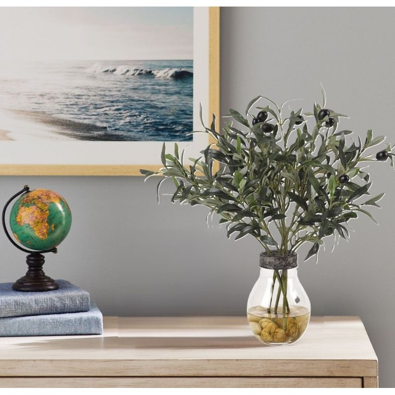 Small globe and faux olive plant in vase on a light wood table, with ocean photo in background.