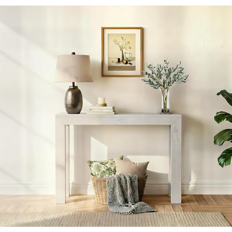 Modern console table with lamp, framed art, and vase with greenery in a bright living room.
