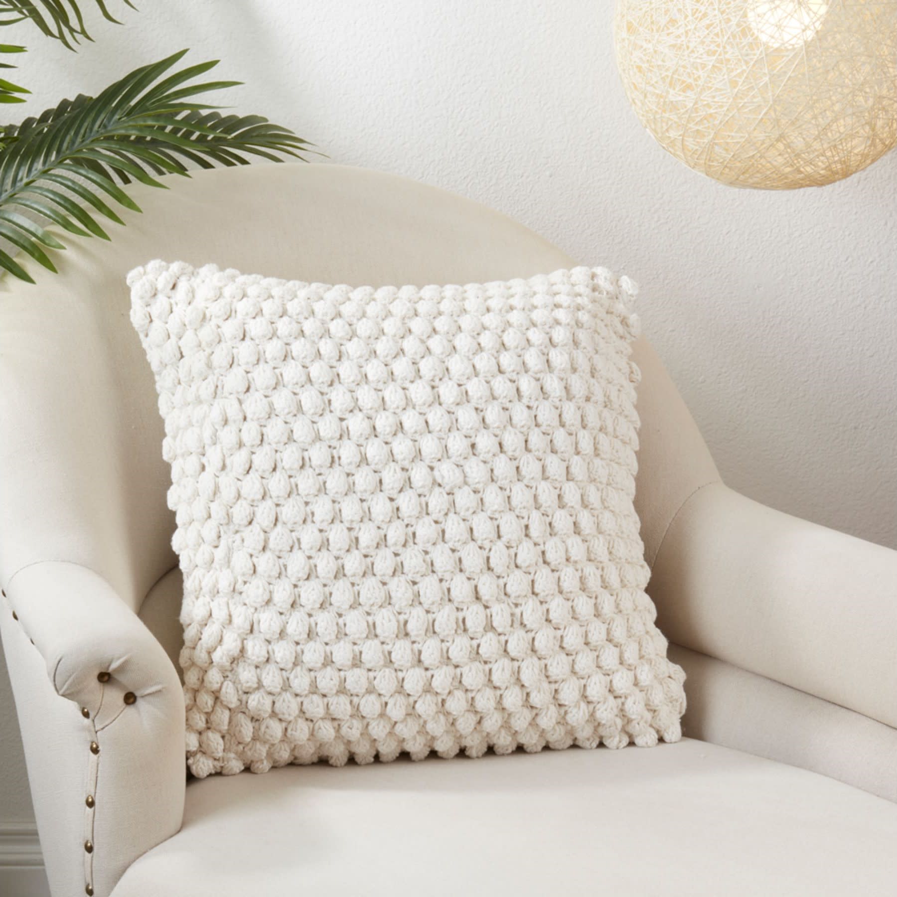 Textured cream pillow on a light armchair, with a plant and woven lamp nearby.