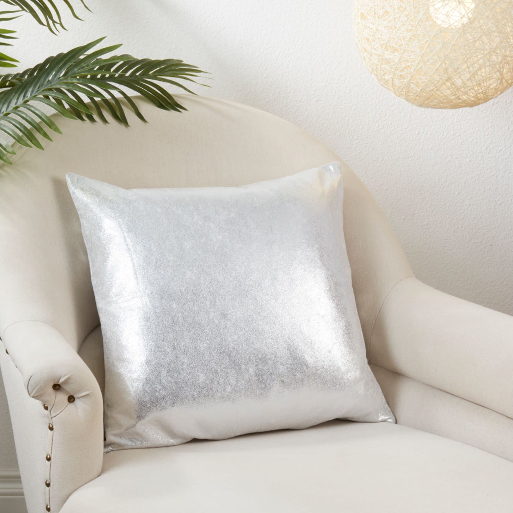 Silver decorative pillow on cream armchair in a modern setting.