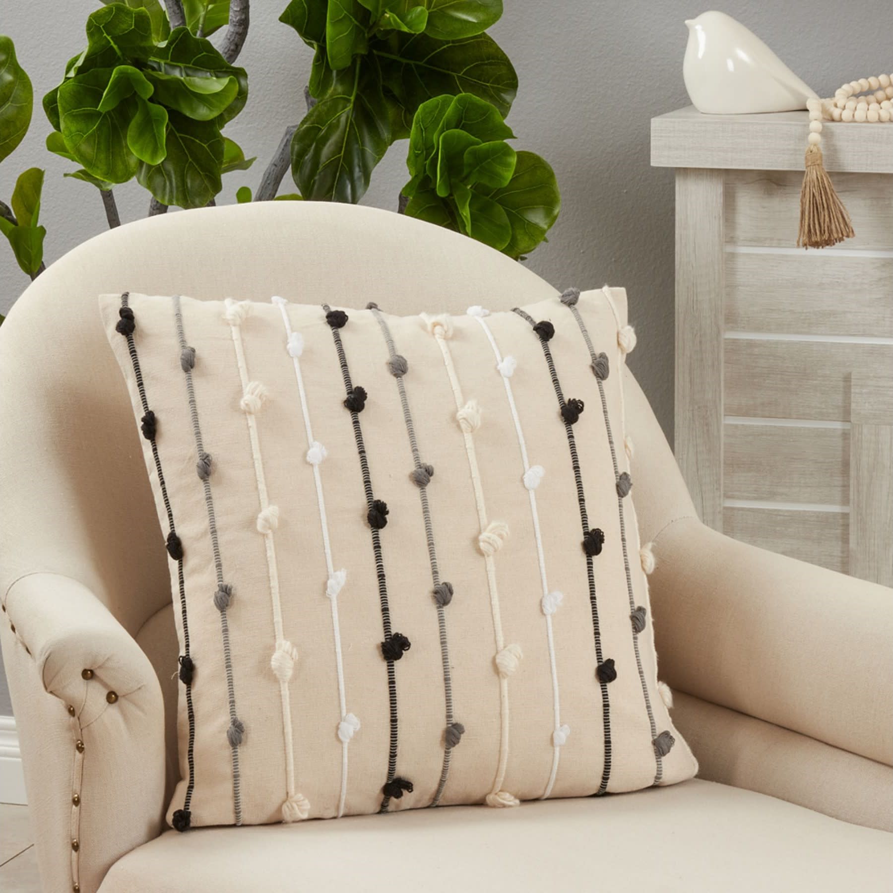 Beige decorative pillow with textured vertical stripes in black, white, and gray on a cream armchair.