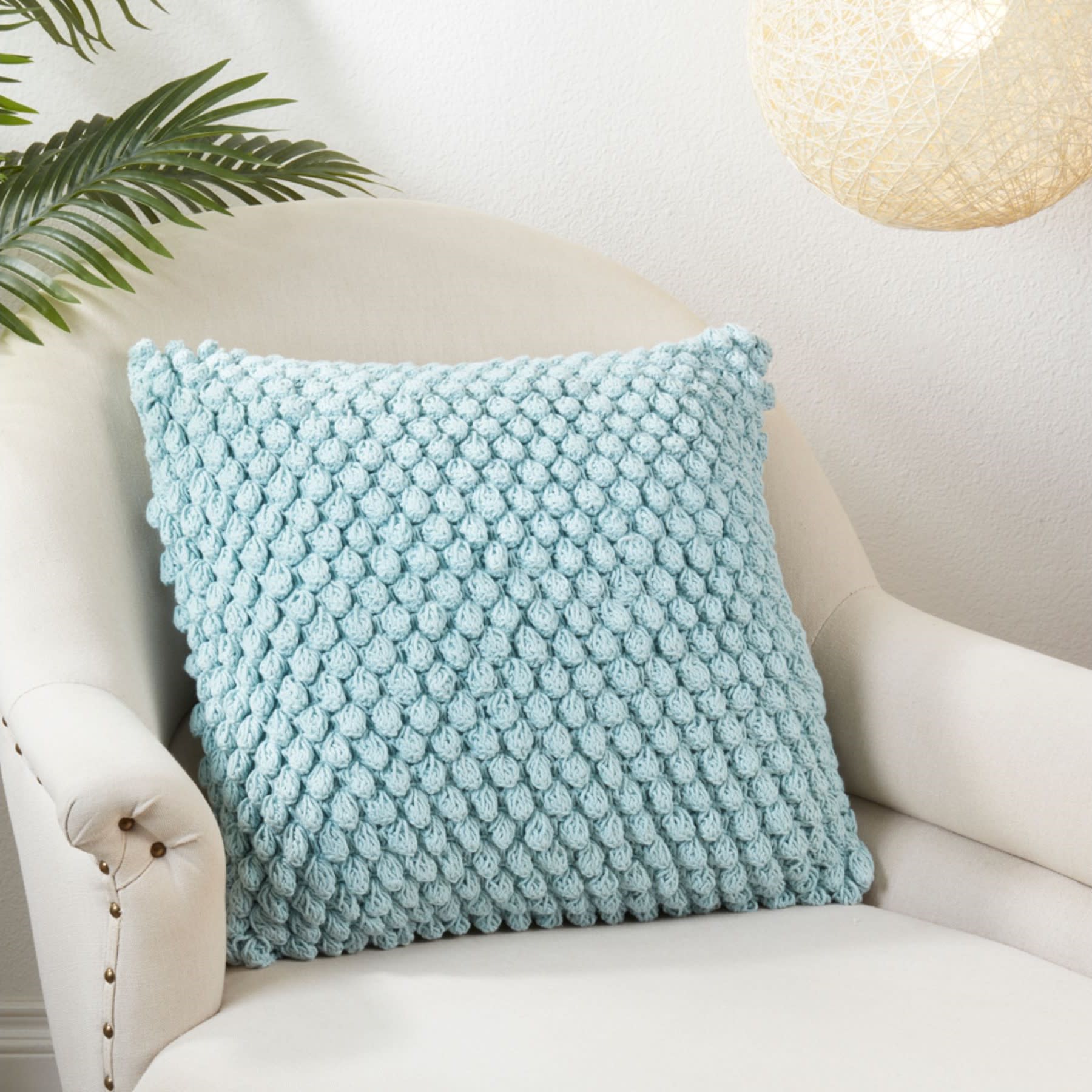 Light blue textured throw pillow on a cream armchair in a cozy living space.