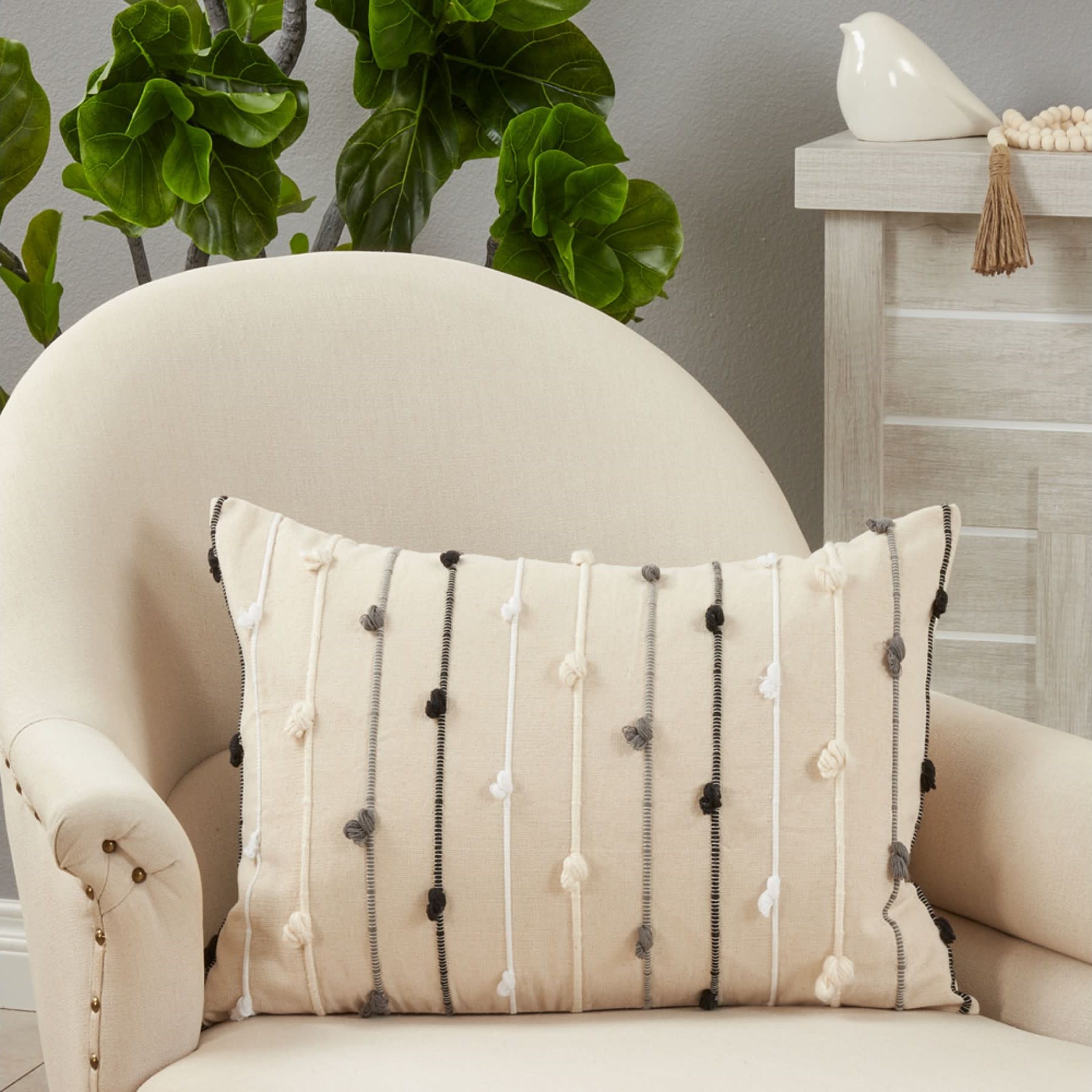Beige accent pillow with vertical yarn stripes and knots on an armchair in a modern living room.