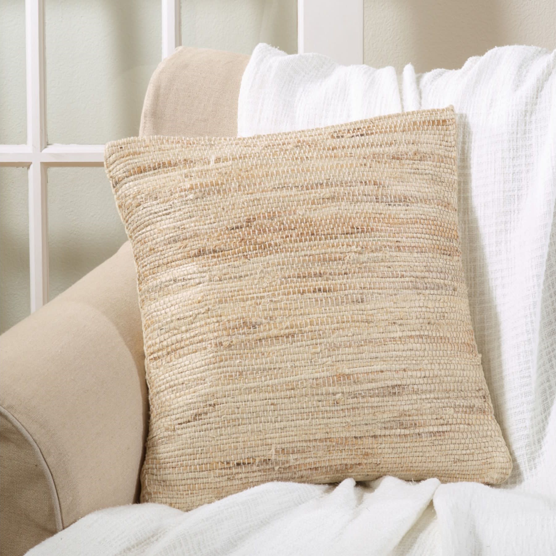 Woven beige throw pillow on a beige sofa with a white blanket.