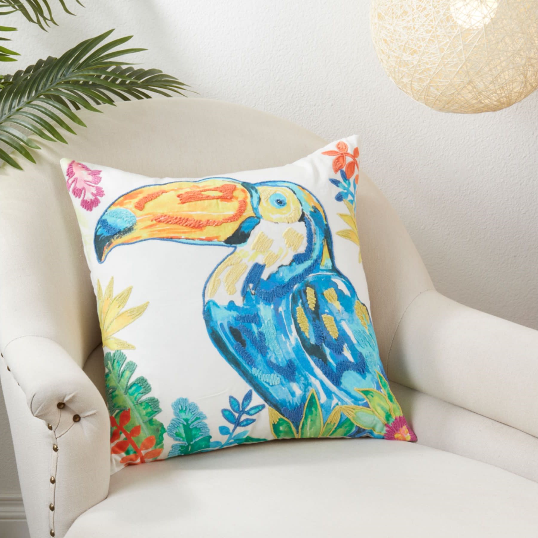 Colorful toucan pillow on a cream armchair with tropical decor.