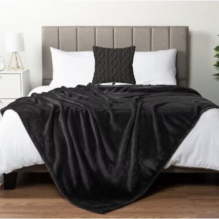 Black throw blanket draped over a made bed with a dark accent pillow.
