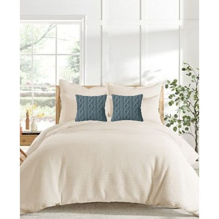 Beige bed with white pillows and two blue decorative pillows in a bright bedroom.