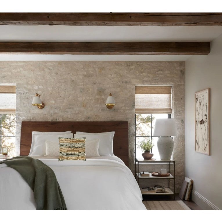 Modern bedroom with wood beams, neutral stone wall, and a bed with white bedding and a textured pillow.