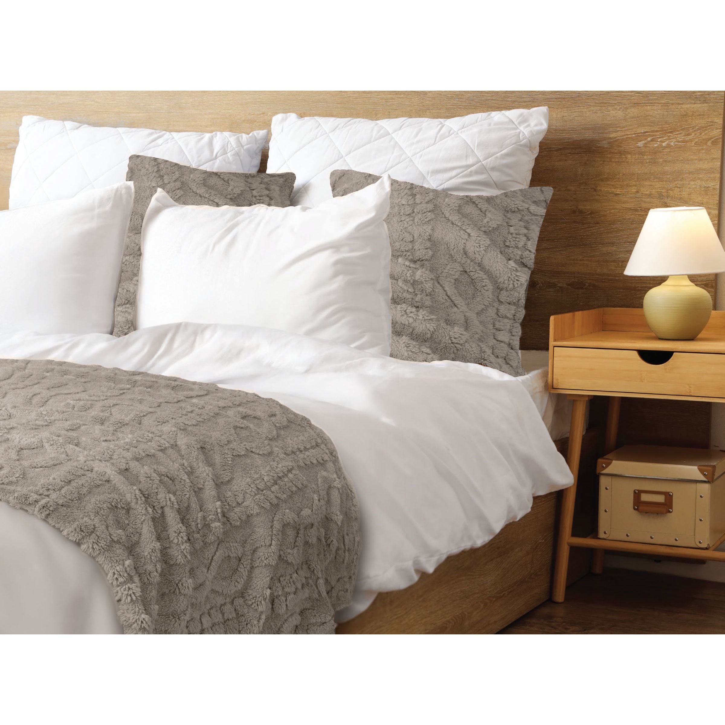 Bed with textured gray accent pillows and throw blanket, wooden headboard, and nightstand with lamp.