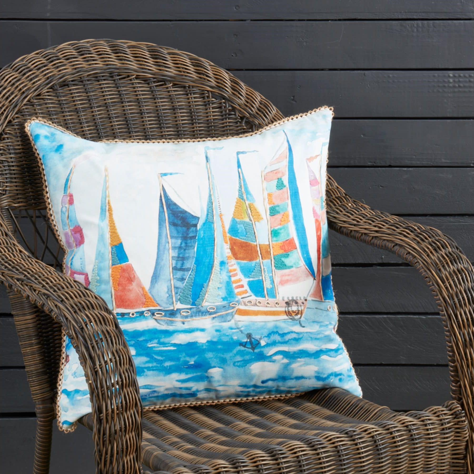 Decorative pillow with colorful sailboat design on a wicker chair.