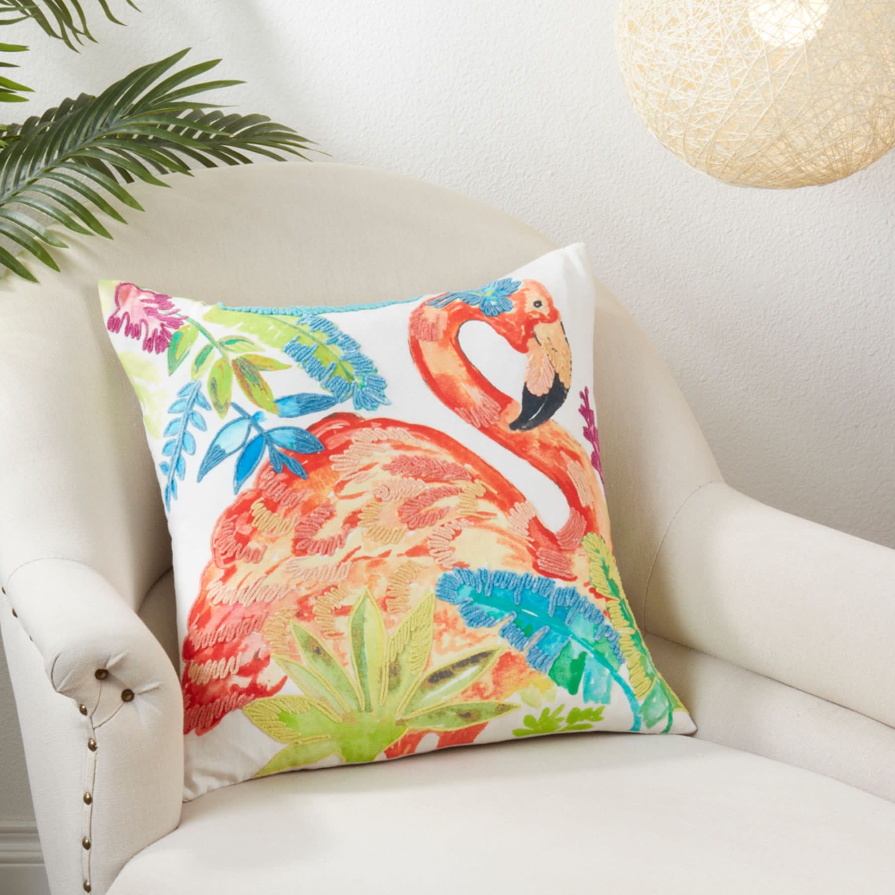 Decorative pillow with a colorful flamingo and tropical leaves on a white chair.