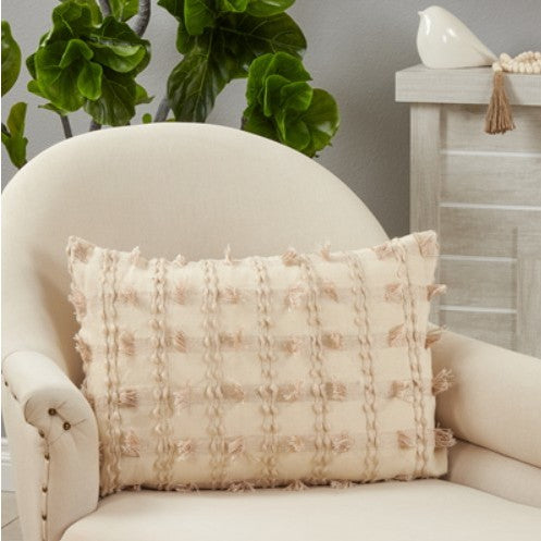 Textured beige throw pillow on cream armchair with green plant in background.