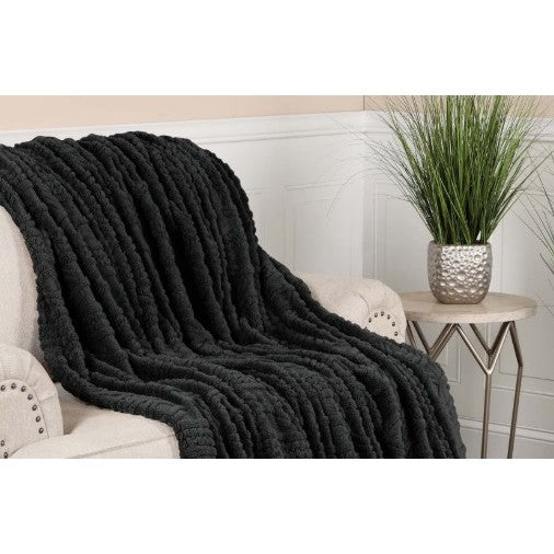 Black textured throw blanket draped over a beige armchair near a small side table with a potted plant.
