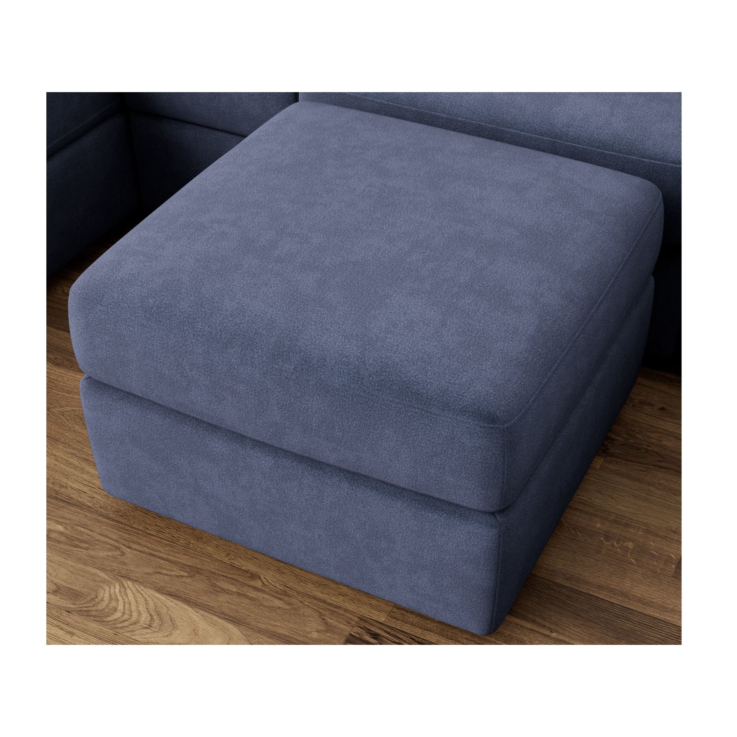 Blue fabric ottoman with soft edges on wood floor, part of sectional sofa.