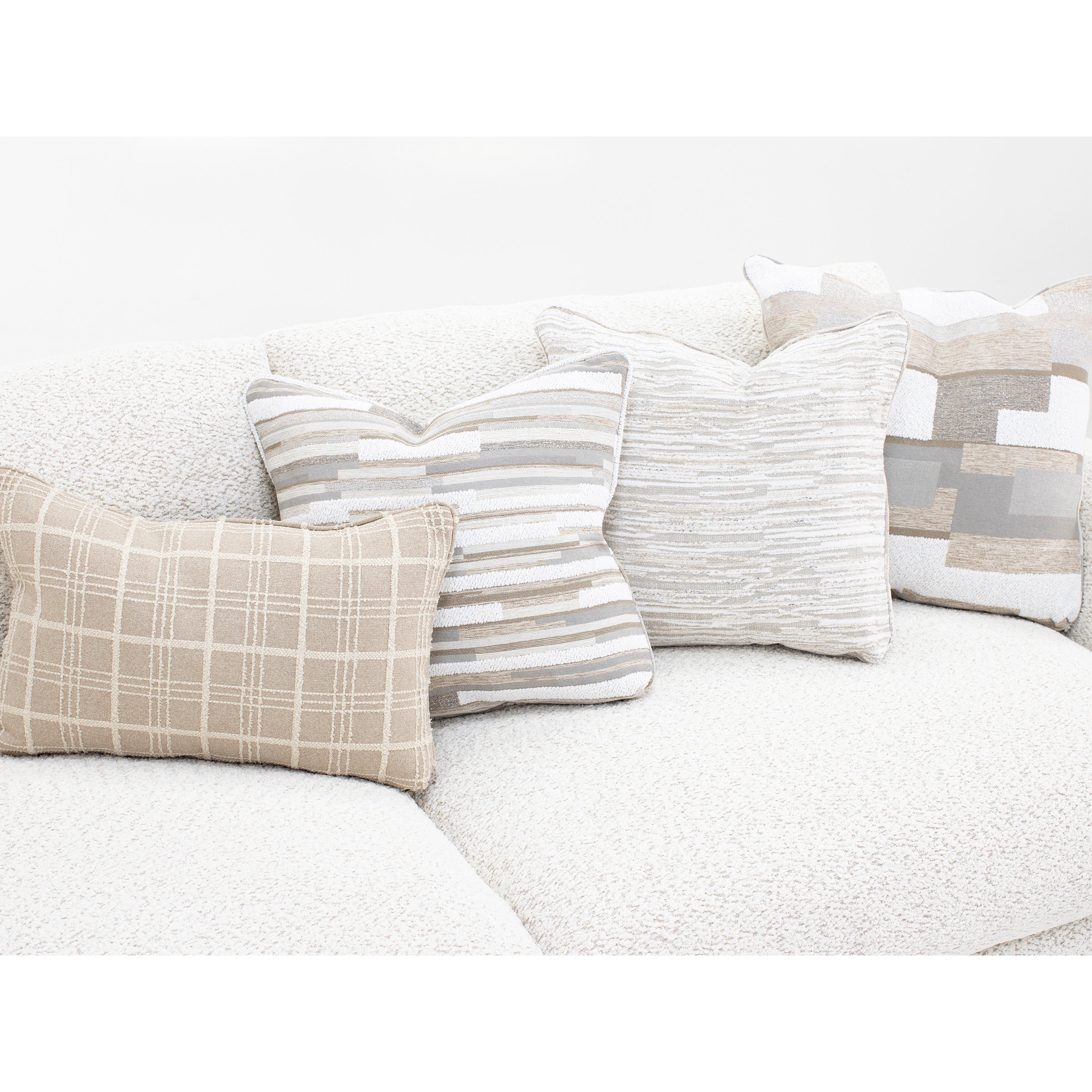 Four neutral decorative pillows with geometric patterns on a light textured sofa.