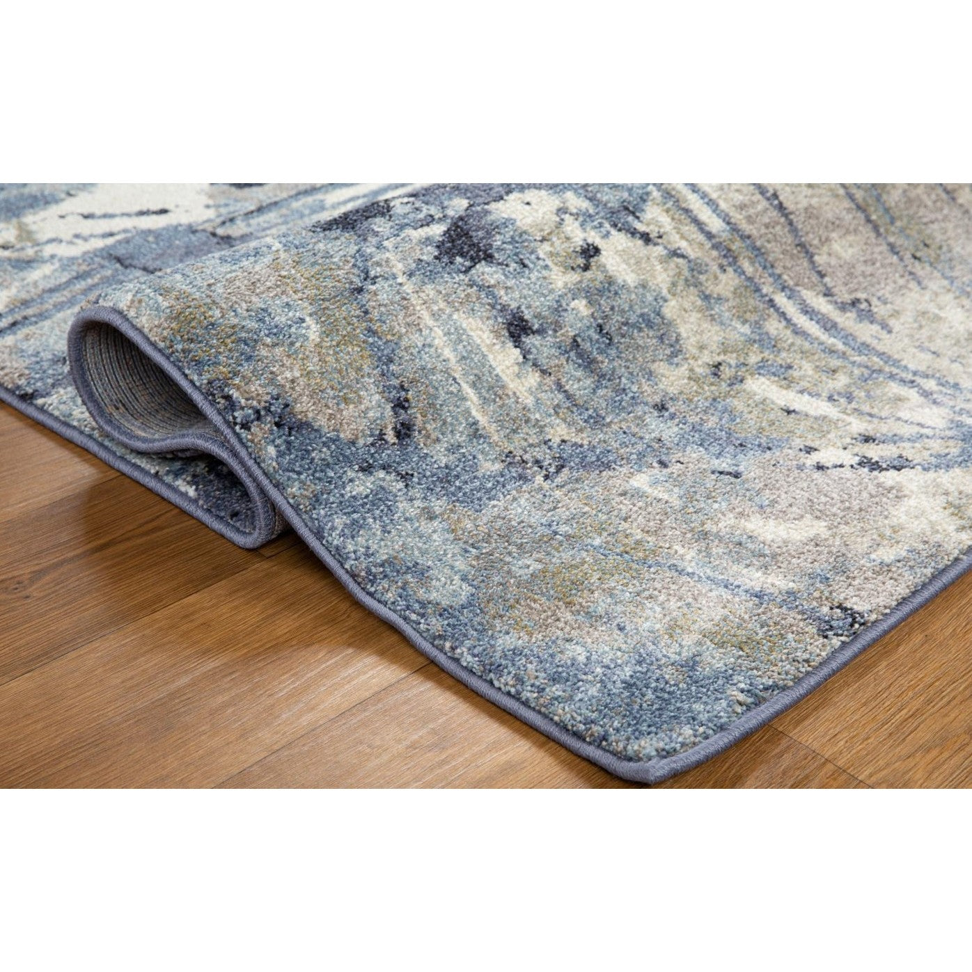 Blue and beige patterned rug corner folded on wood floor.