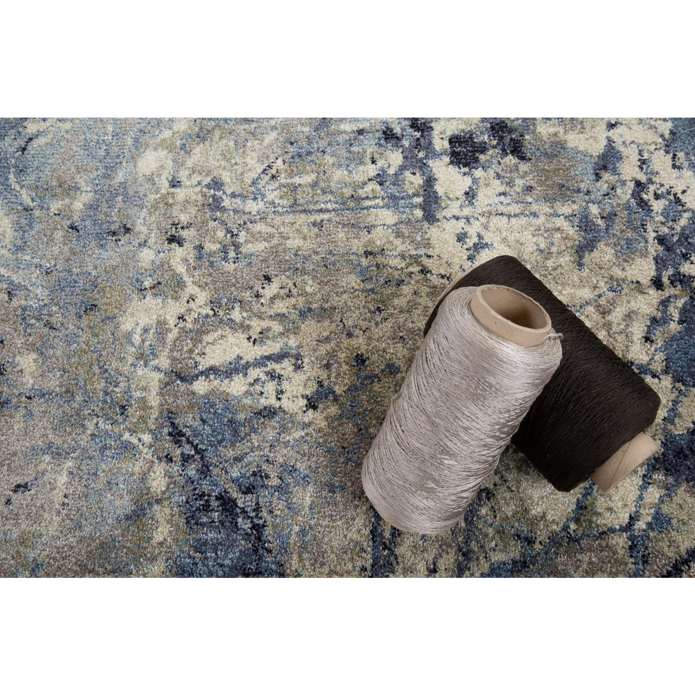 Two spools of yarn rest on a blue and beige patterned carpet.