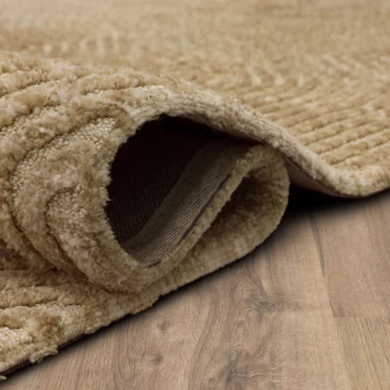 Close-up of a beige textured rug corner folded over on a wood floor.