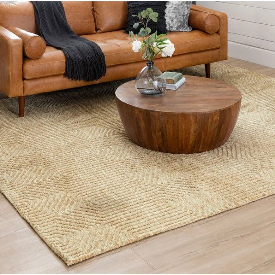 Tan leather sofa and round wooden coffee table on a beige textured rug in a modern living room.