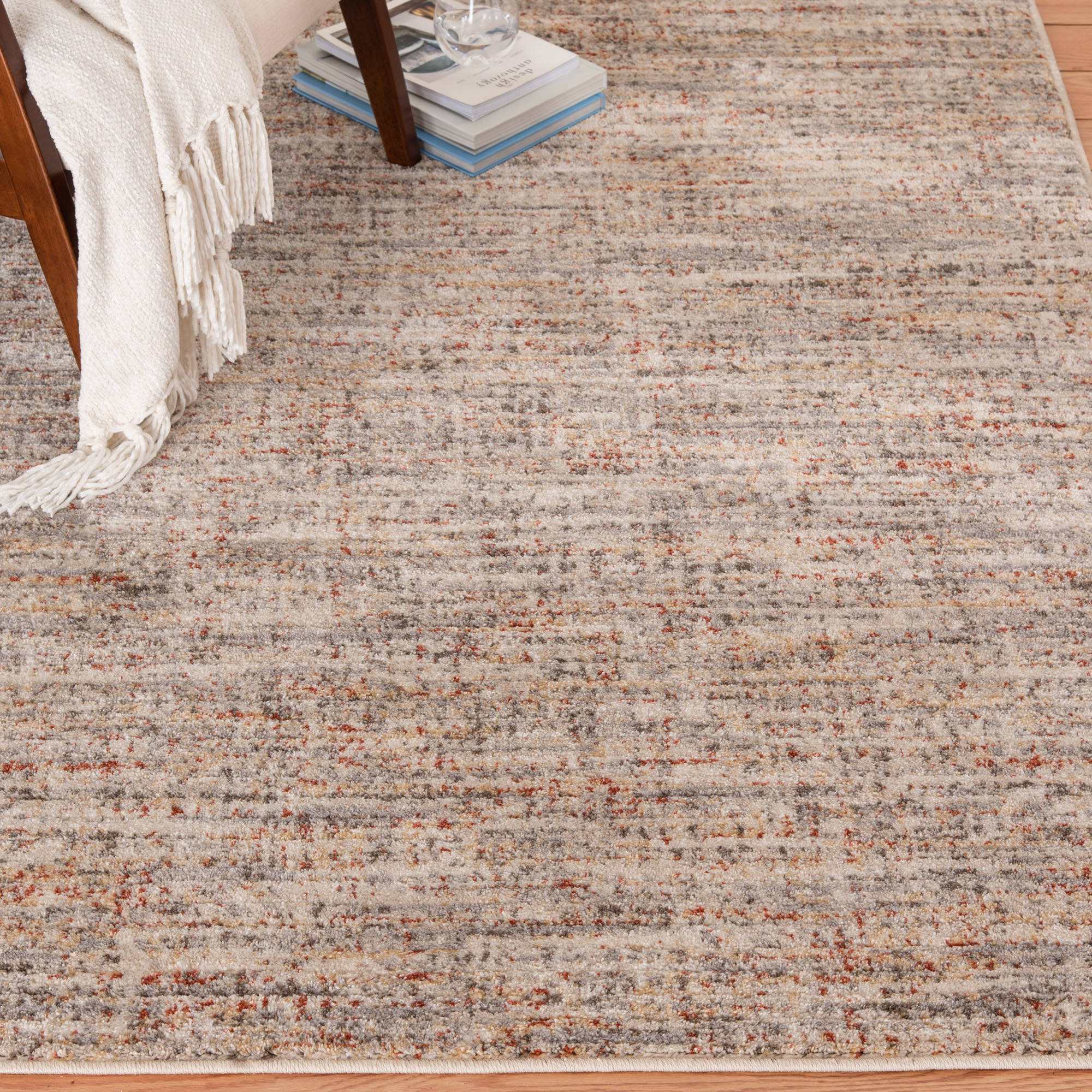 Modern area rug with muted gray and beige tones, partially shown under a chair with books.