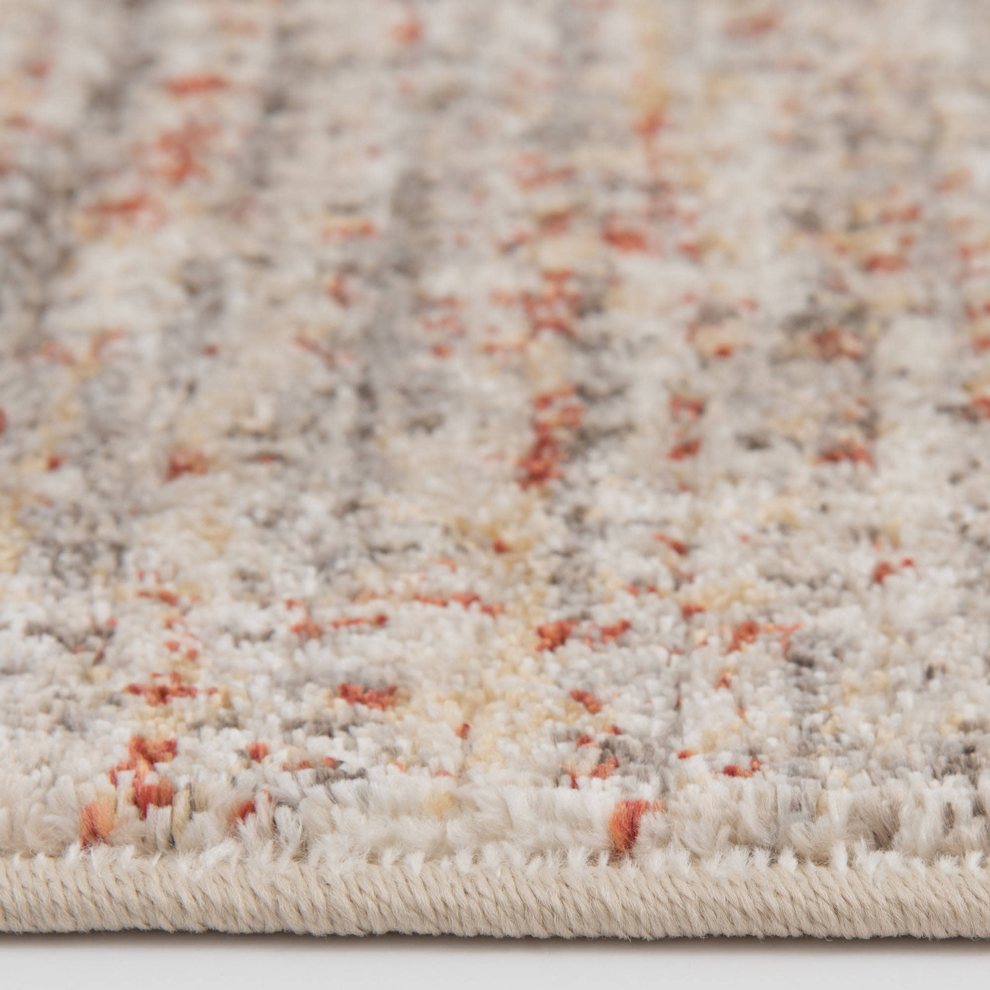 Low-angle closeup of a textured area rug with beige, gray, and rust color accents.