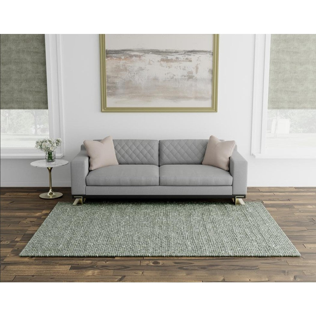 Modern living room with a gray sofa, two pillows, abstract art, and a green area rug.