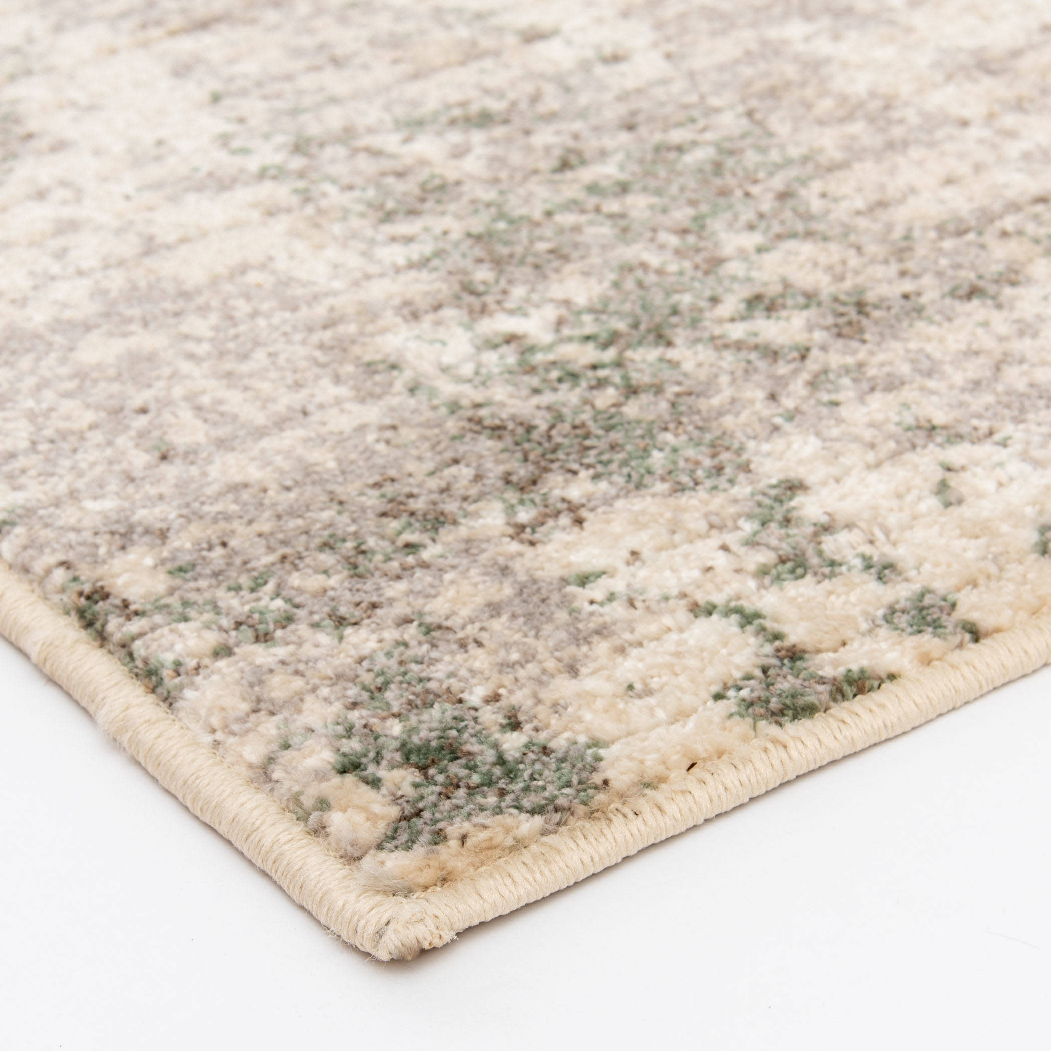 Close-up of a textured area rug with a beige and green pattern, showing the edge detail.