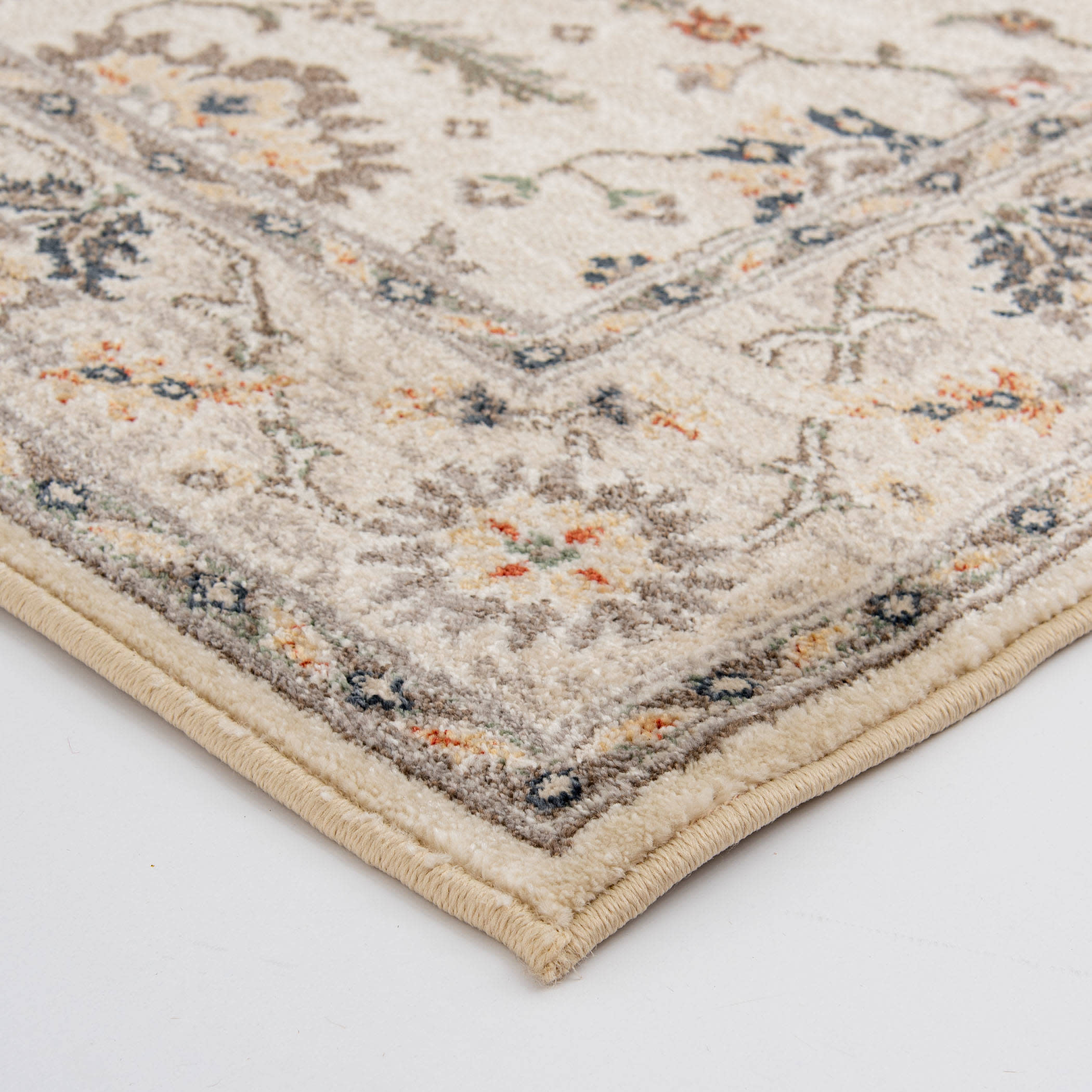 Close up of a beige area rug corner with a floral border pattern.