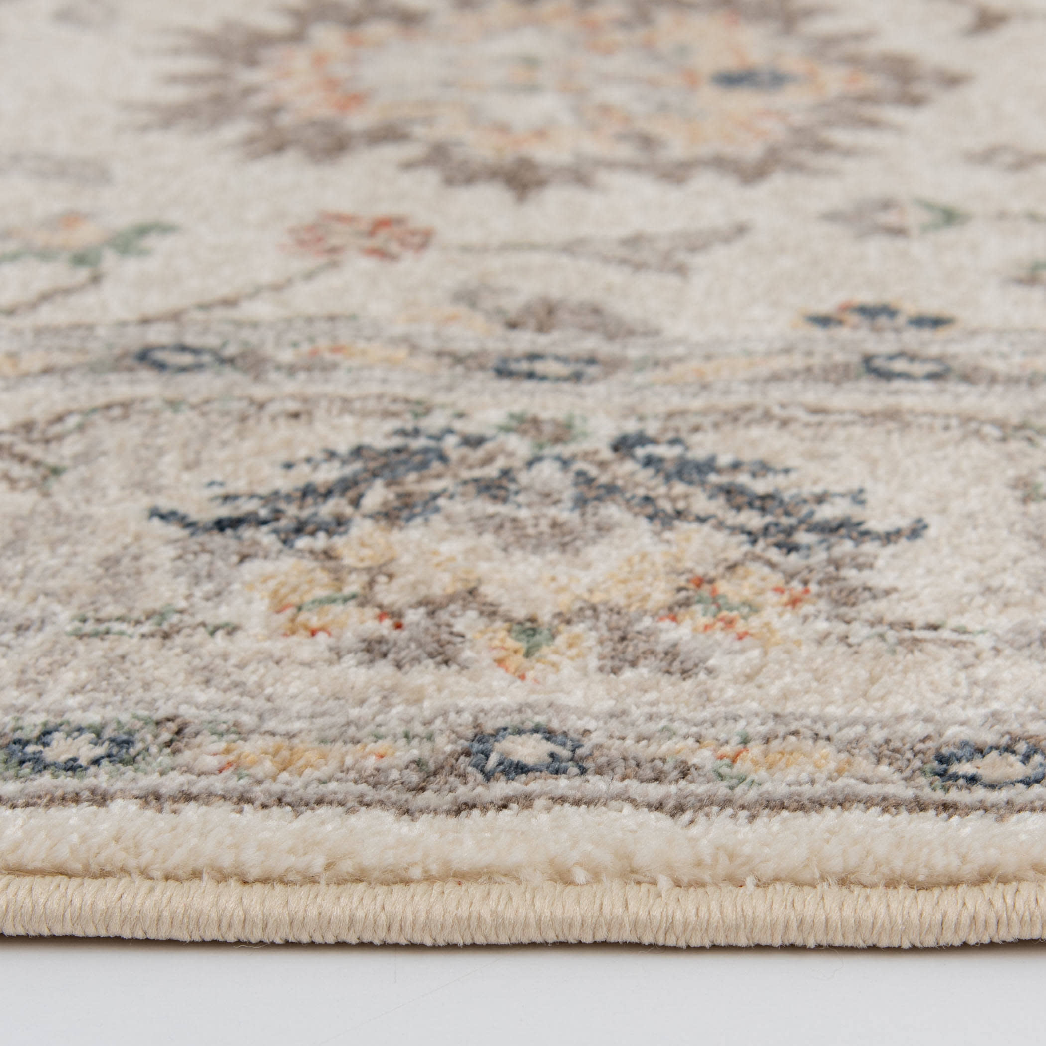 Close-up of a beige area rug showing plush texture and a subtle traditional pattern.