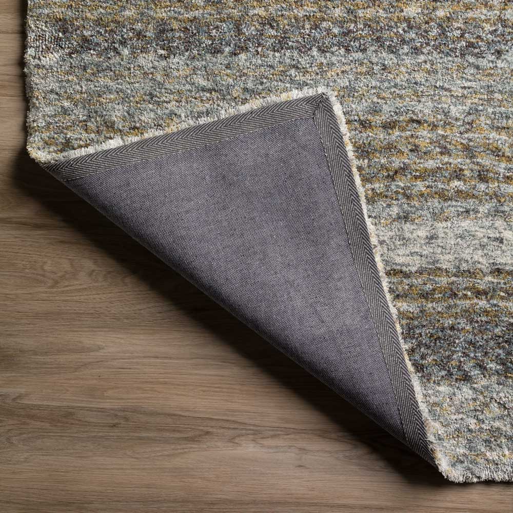 Corner of textured area rug folded over to show backing on wood floor.