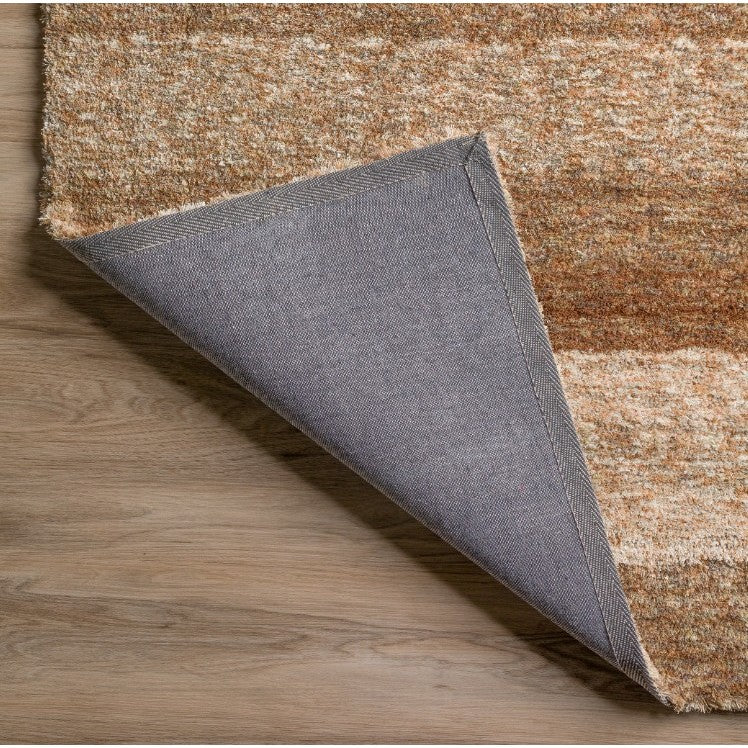 Corner of a tan and brown area rug folded to show backing on wood floor.