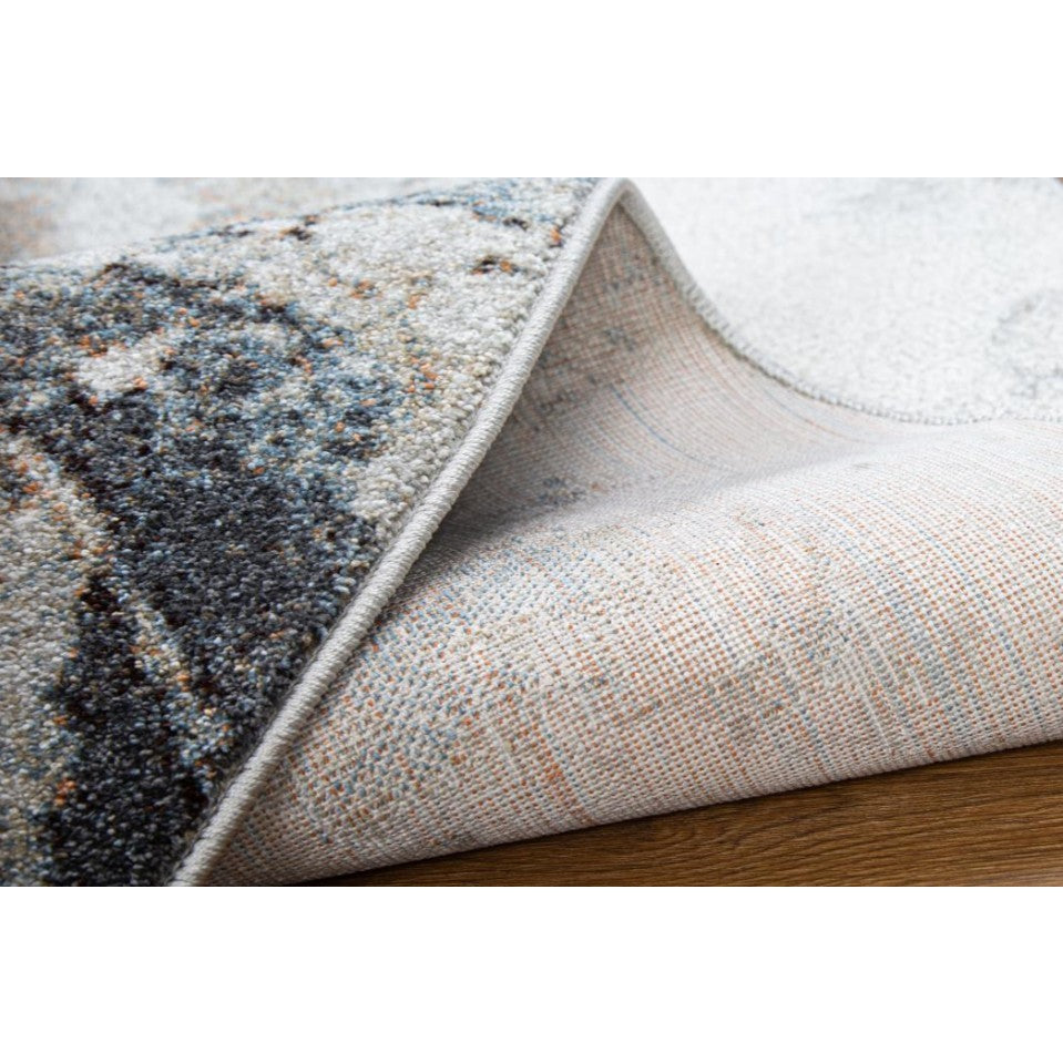 Close-up of an area rug corner lifted to show backing and surface texture.